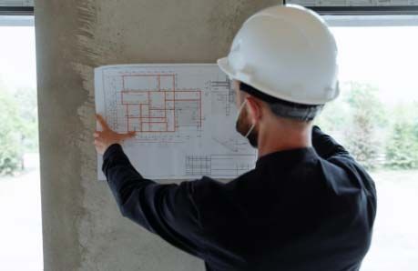 Person in hard hat examines blueprints on a construction site.