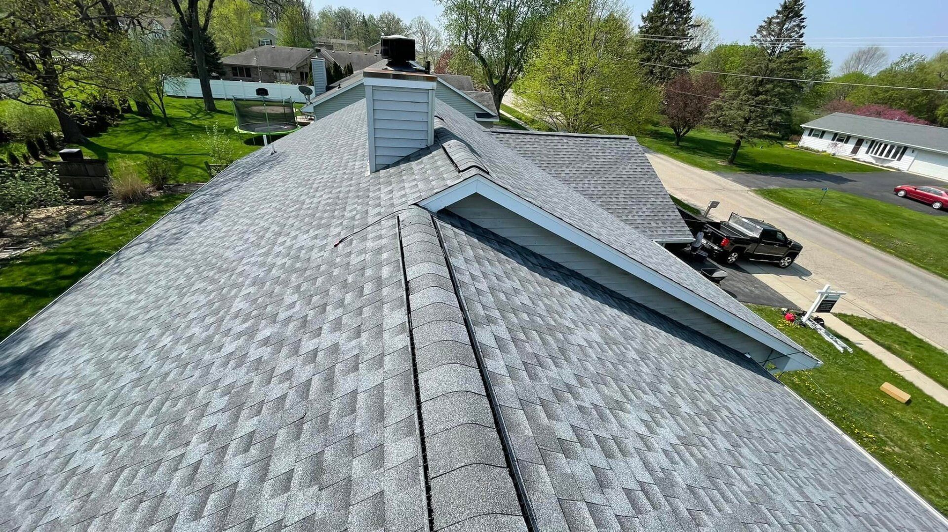 Gray shingled roof with chimney, in a residential area.