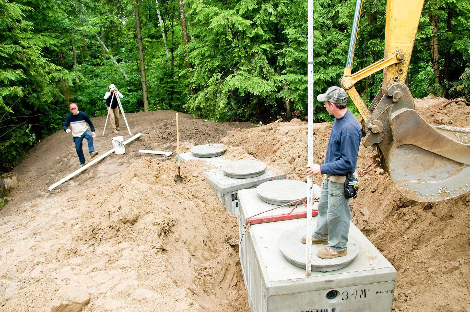 A man is standing next to a septic tank in a dirt field.