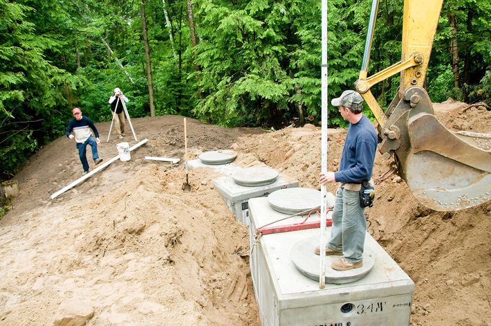 A man is standing next to a septic tank in a dirt field.