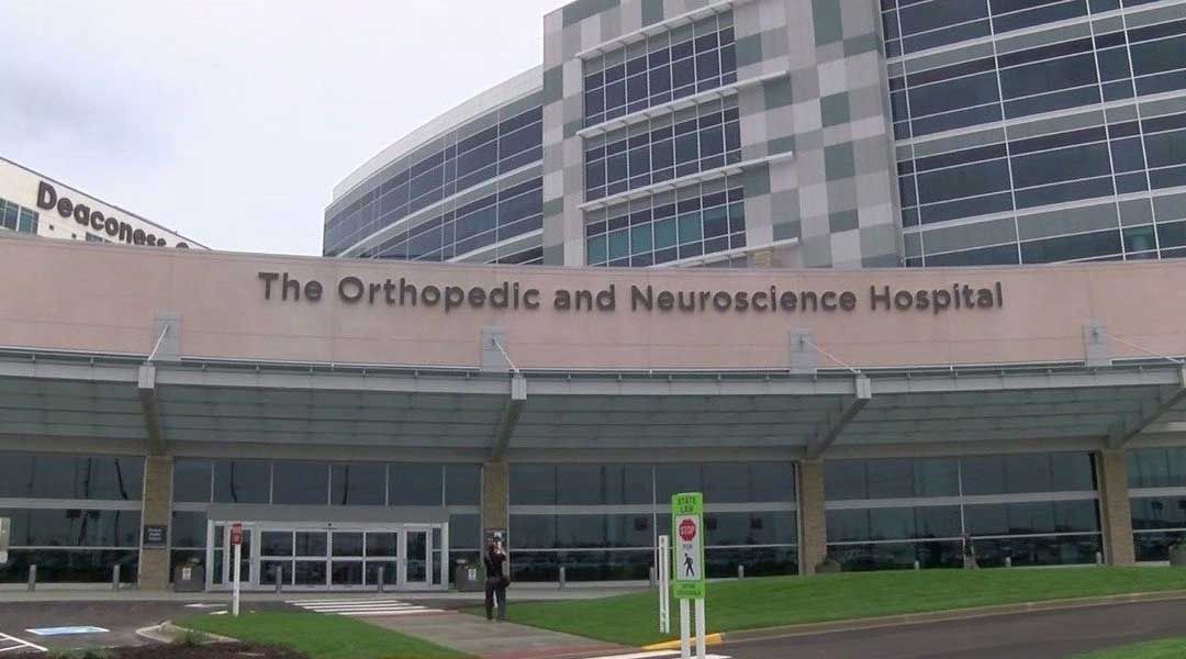 Exterior of The Orthopedic and Neuroscience Hospital. Glass entrance, large building with text, overcast sky.