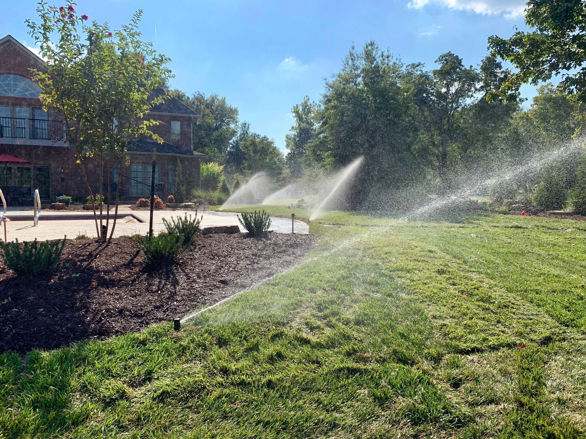 Sprinklers watering green lawn in front of a building on a sunny day.