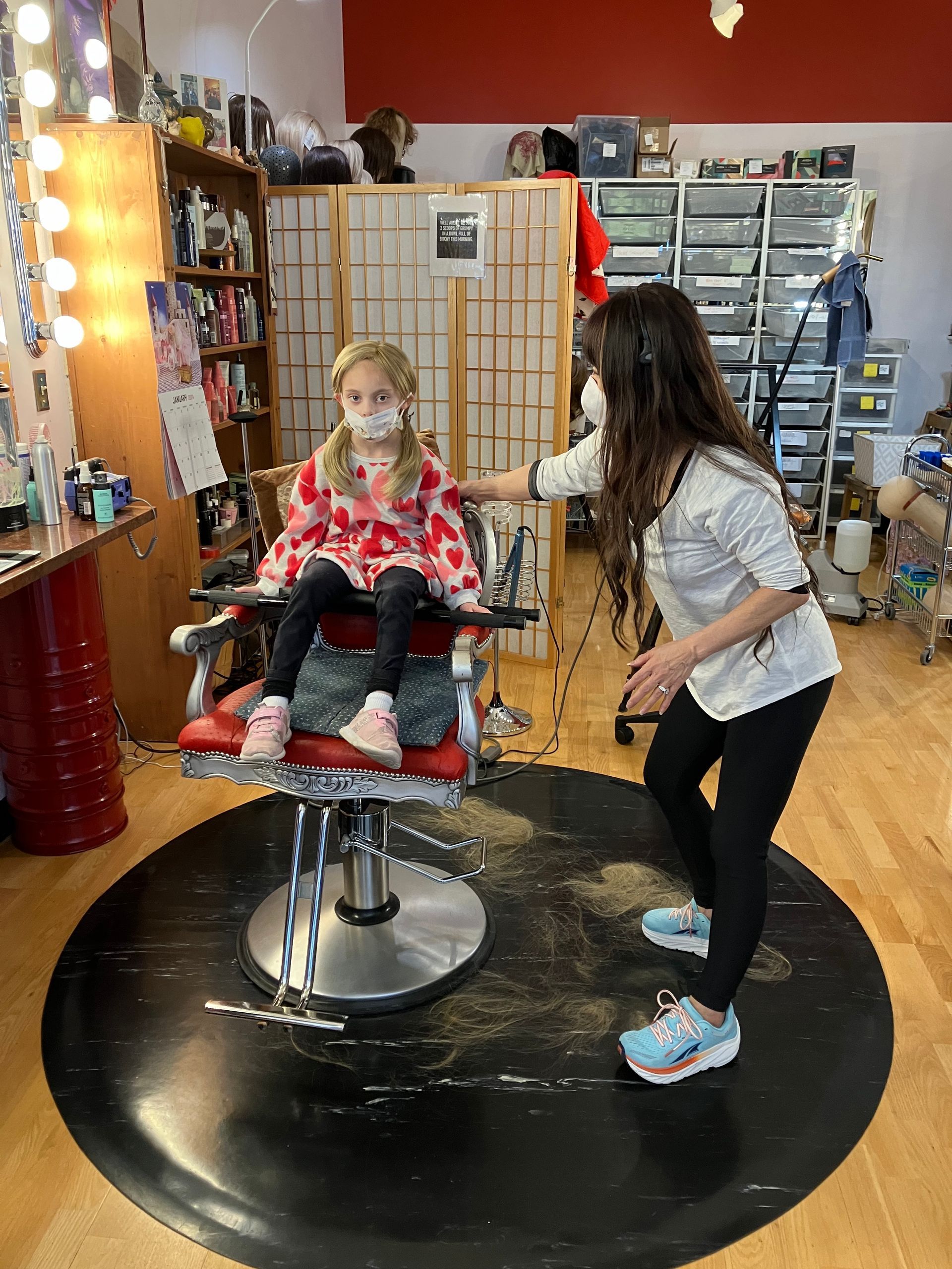A woman is standing next to a little girl sitting in a chair.