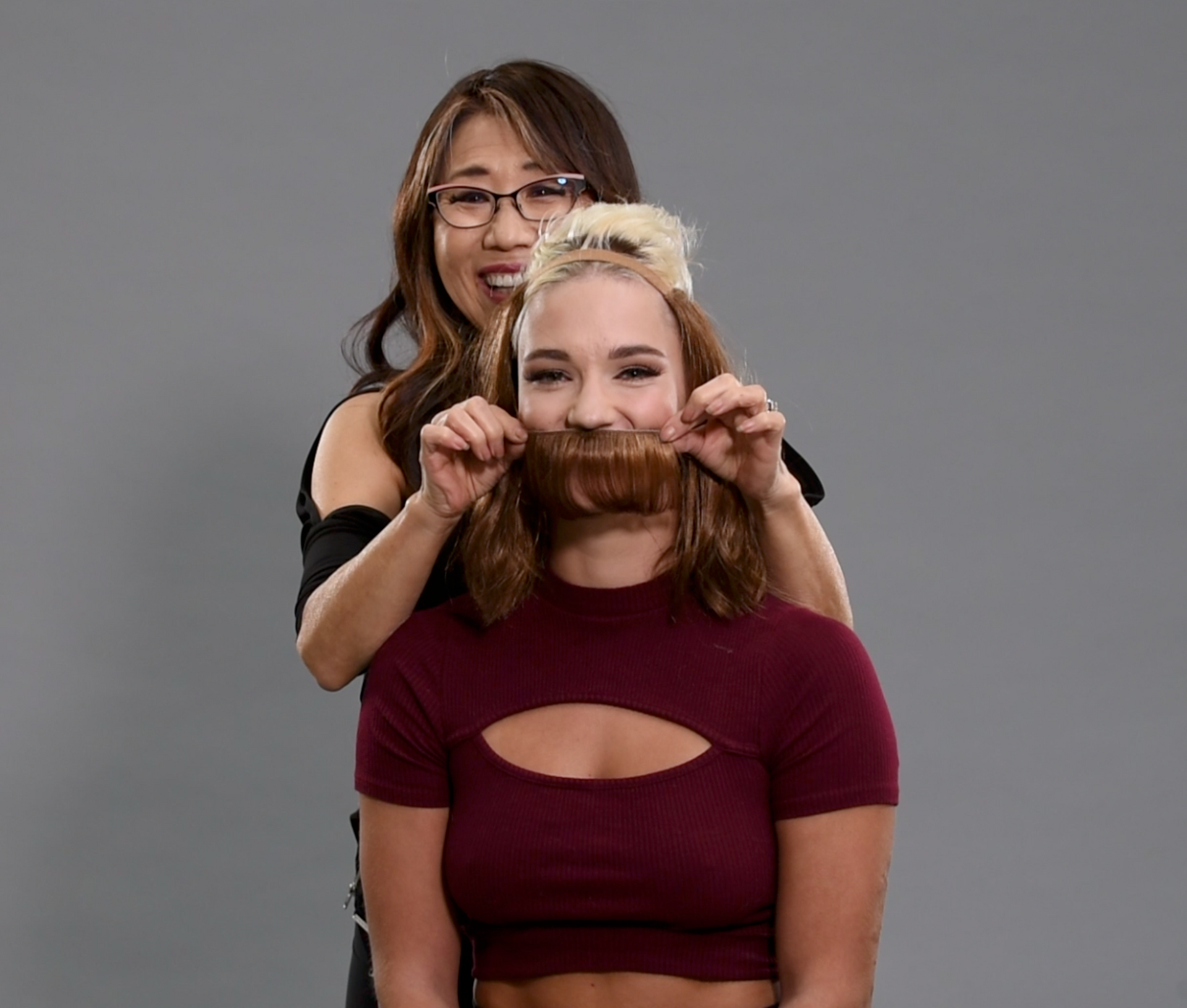 A woman is putting a fake beard on another woman 's face.