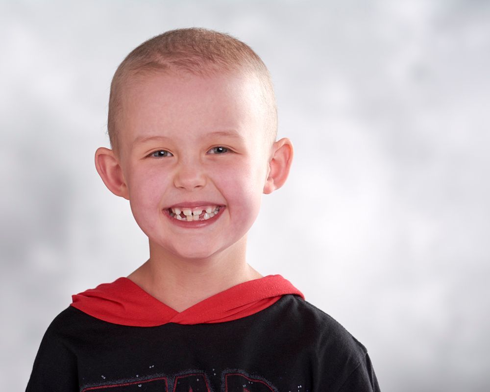 A young boy wearing a black shirt and a red hoodie is smiling for the camera.
