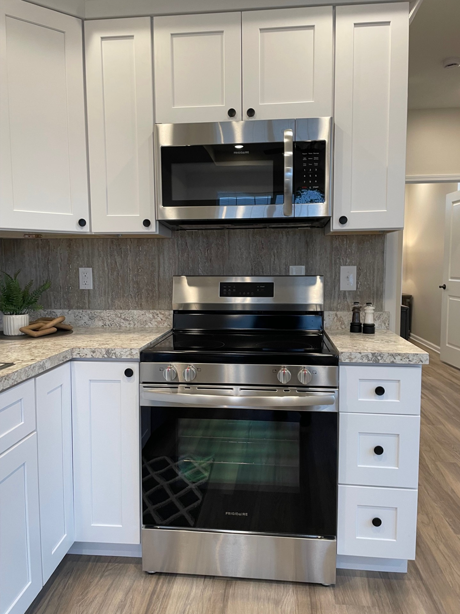 Stainless steel appliances in a white kitchen. Microwave above the oven. Counter with a backsplash.