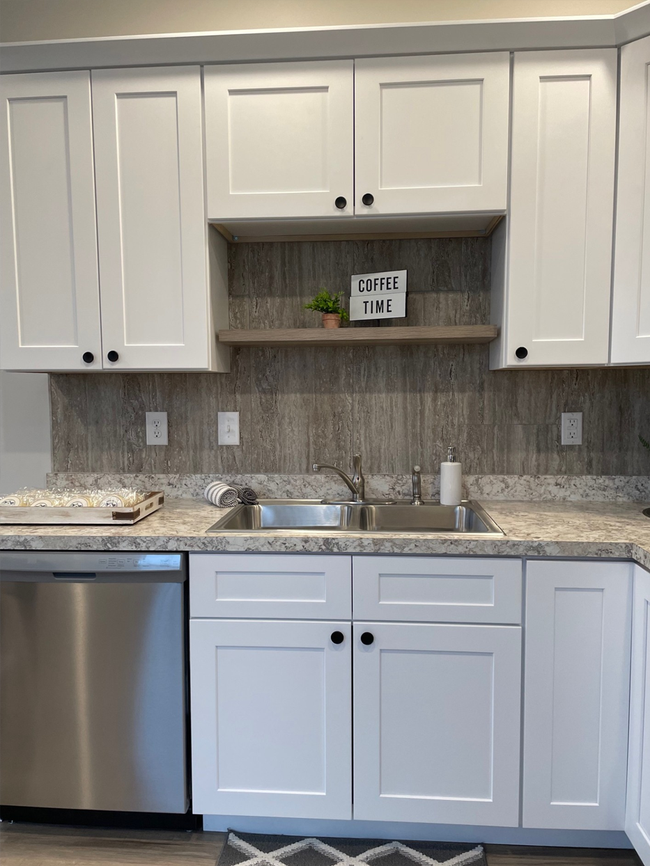 White kitchen cabinets with black knobs, stainless steel appliances, and a patterned backsplash.