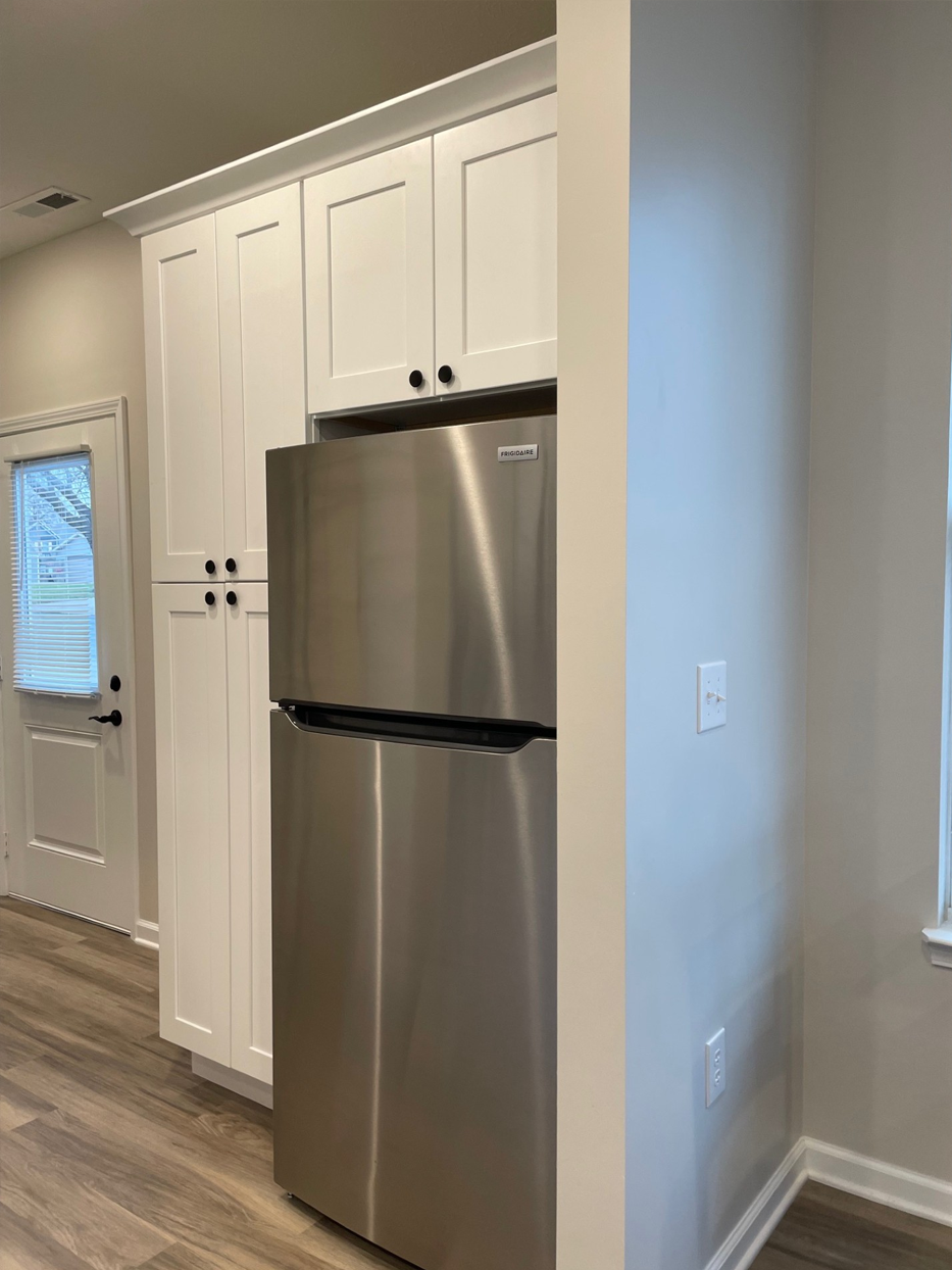 Stainless steel refrigerator next to white cabinets. Light-colored floor and door.