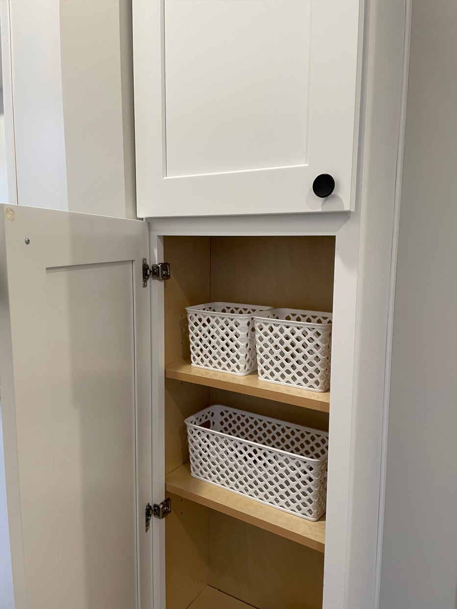 White pantry cabinet with open door; shelves hold three woven storage baskets.