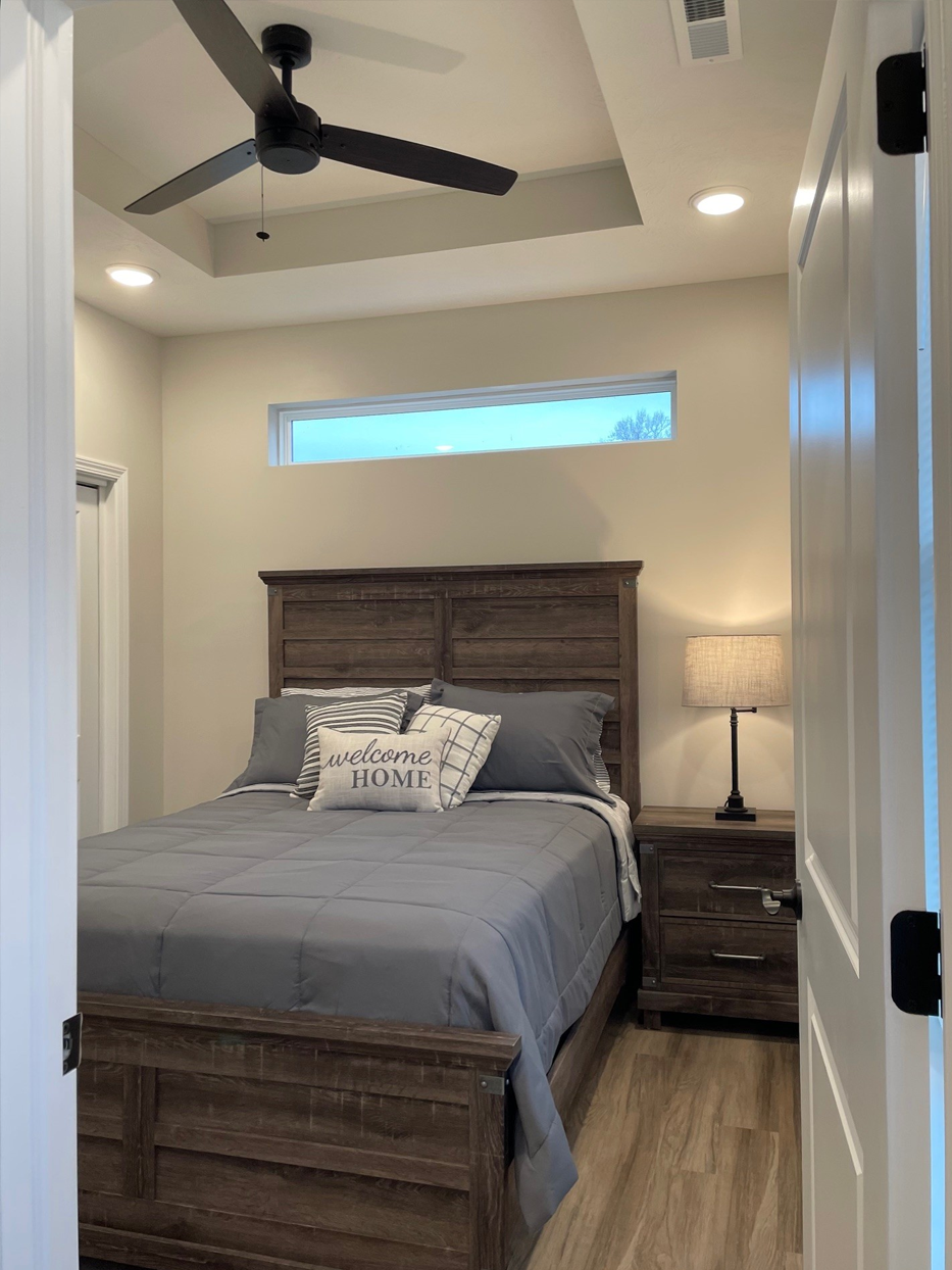 Bedroom with a wooden bed frame, gray bedding, and a ceiling fan.