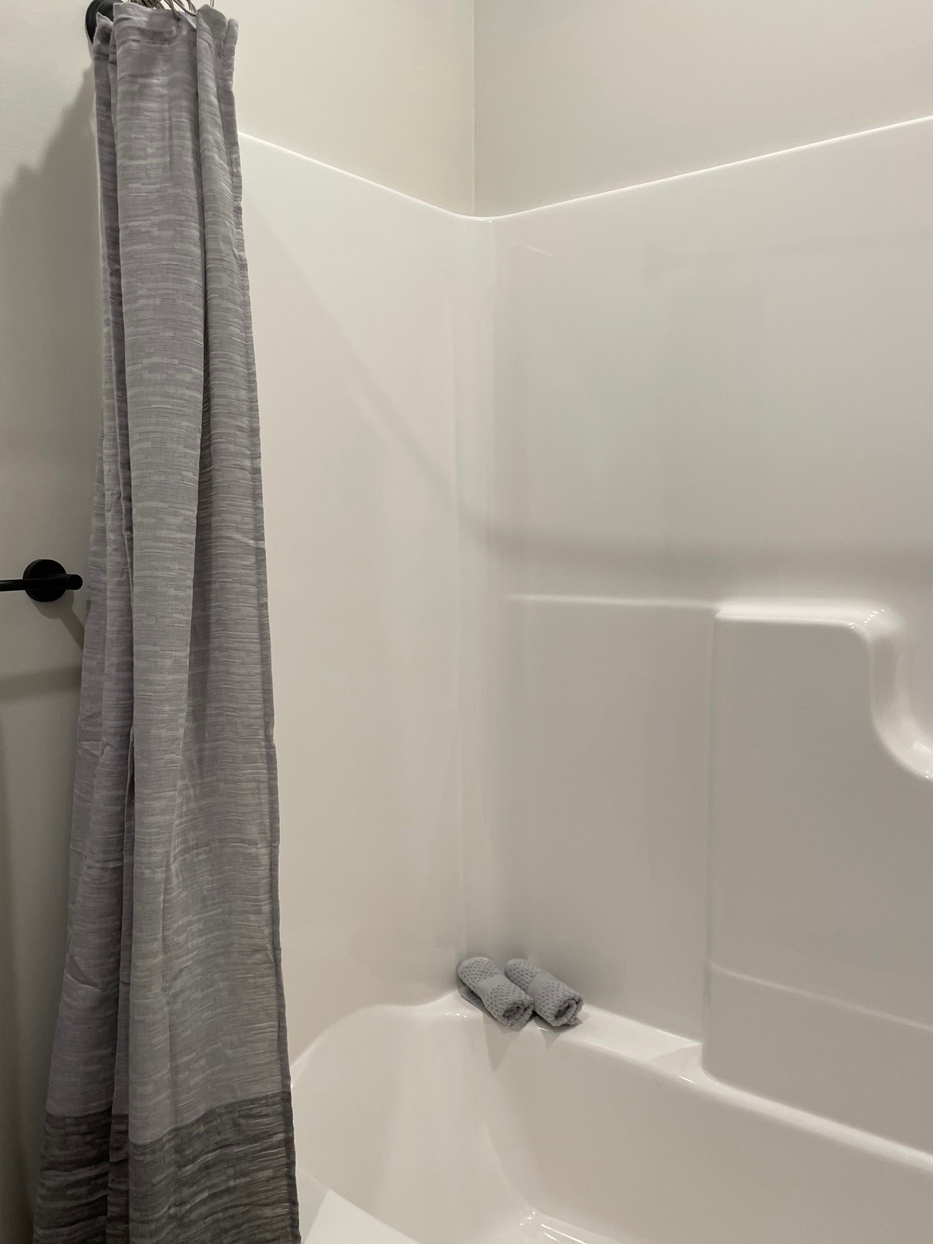 A white shower stall with a gray shower curtain and a folded gray towel in the bathtub.
