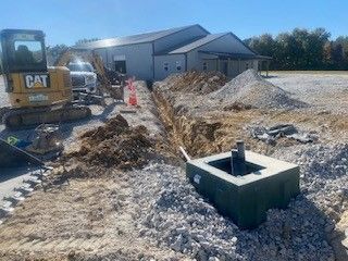 A cat excavator is digging a hole in the dirt in front of a building.