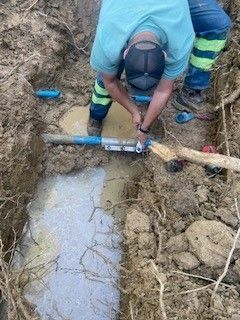 A man is working on a pipe in the dirt.