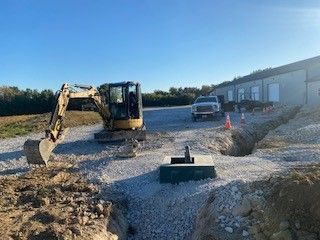 An excavator is digging a hole in the dirt in front of a building.