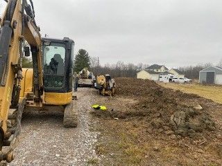A yellow excavator is driving down a dirt road next to a large pile of dirt.