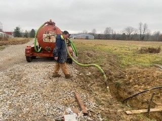 A man is standing next to a vacuum truck on a gravel road.