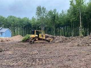 A bulldozer is moving dirt in a field with trees in the background.