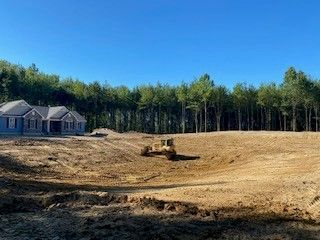 A bulldozer is working on a dirt field in front of a house.