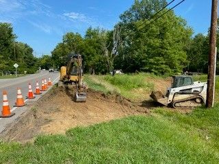 A bulldozer is digging a hole in the grass next to a road.