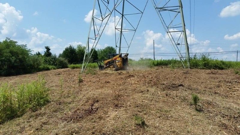 A bulldozer is clearing a field in front of a power tower.