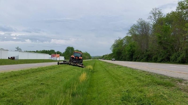 A tractor is mowing grass on the side of a highway.