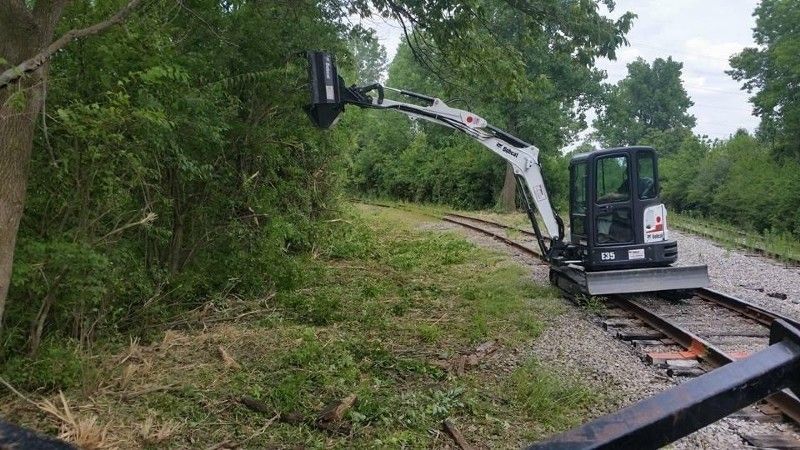 A small excavator is working on train tracks in the woods.