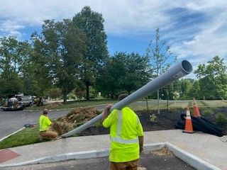 A man in a yellow shirt is carrying a large pipe on his back.
