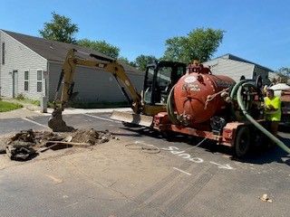 A man is standing next to a vacuum truck and an excavator.