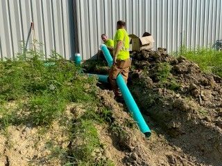 A man is standing in the dirt next to a pile of pipes.