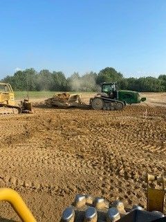 A couple of tractors are working on a dirt field.