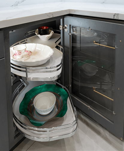 Open corner kitchen cabinet with two chrome pull-out shelves holding dishes and bowls