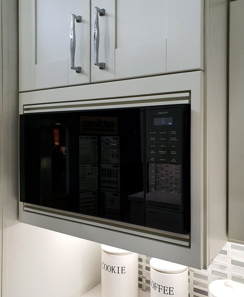 Built-in black microwave in white kitchen cabinets with silver handles
