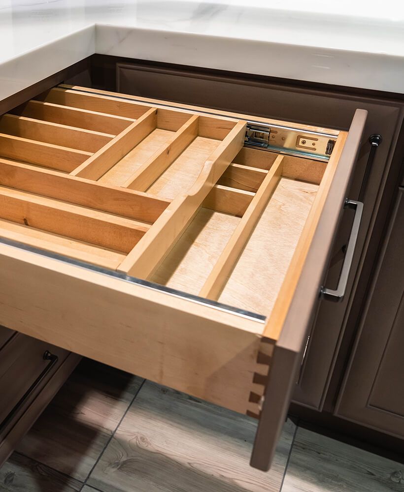 Open kitchen drawer with wooden utensil organizers and a metal handle.