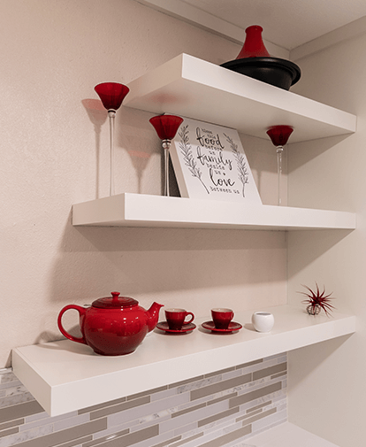 Red decorative shelves with red teapot, cups, bowls, and small framed sign on a tiled wall