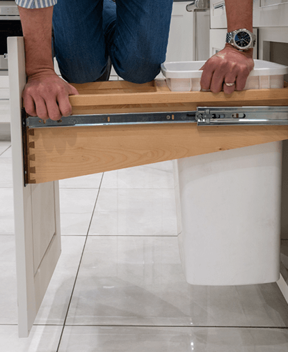 Person kneeling to install a wooden cabinet drawer slide in a tiled room