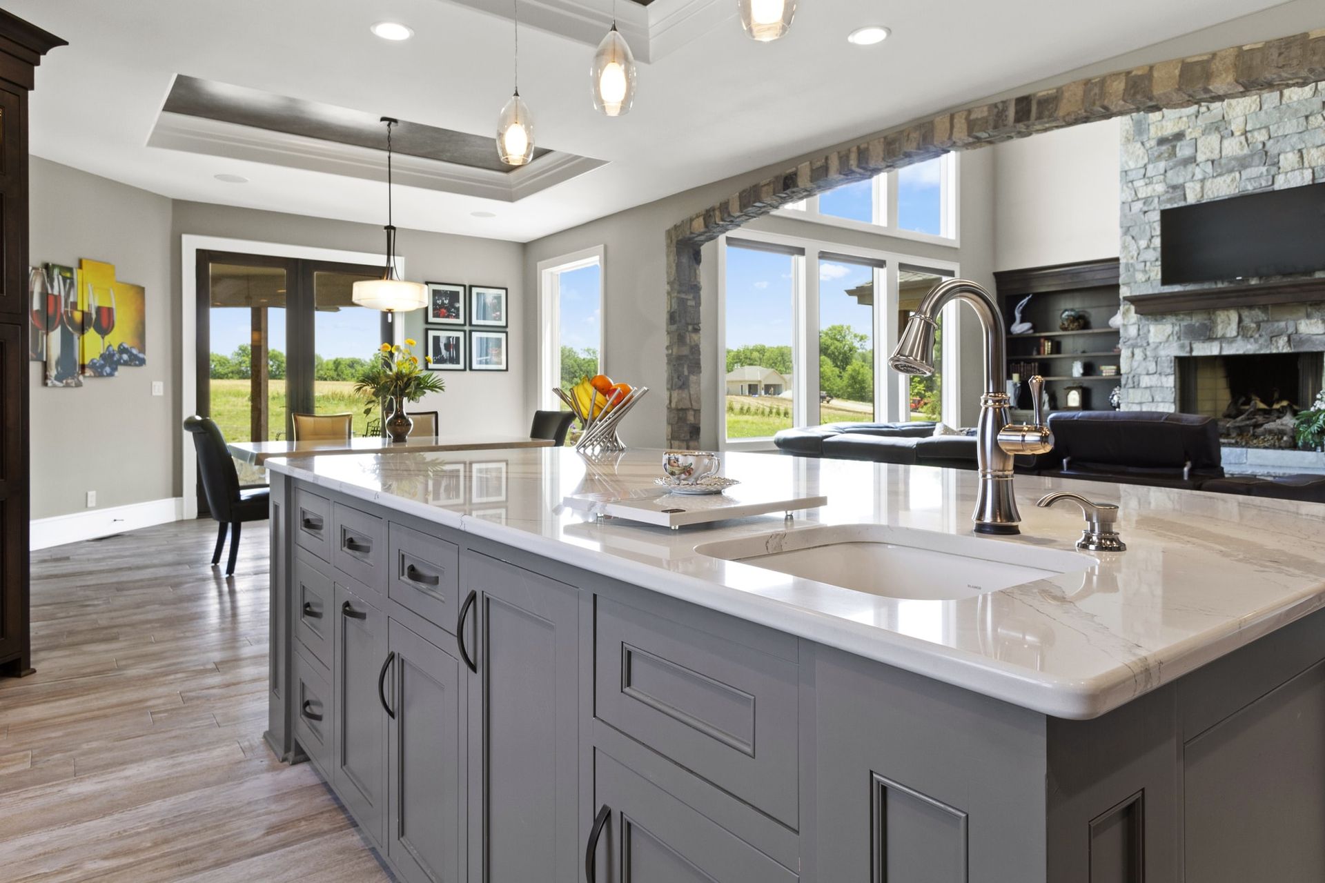 Modern kitchen with large island, white countertops, pendant lights, and bright windows overlooking a view