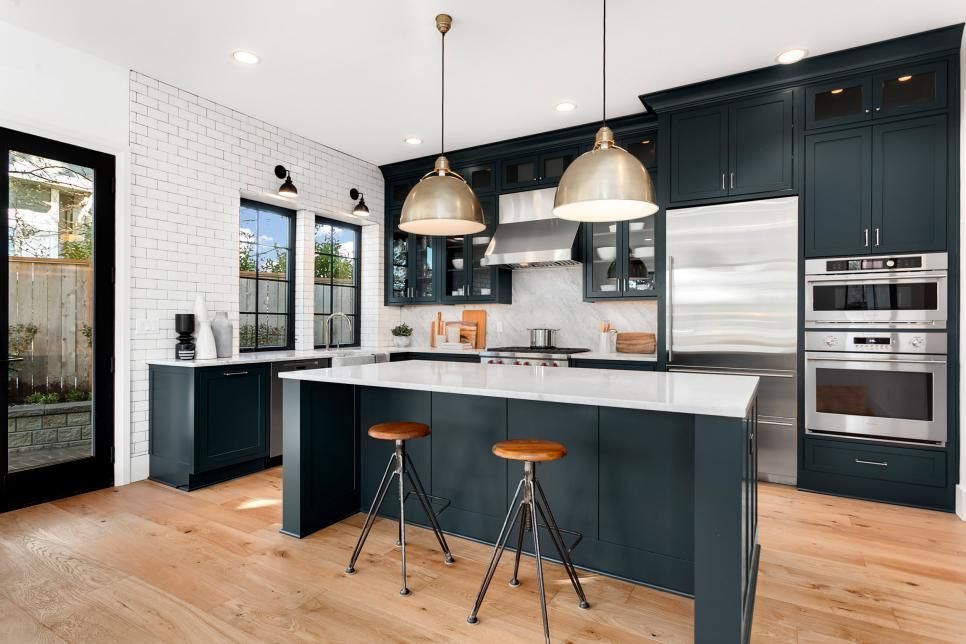 Modern kitchen with dark blue cabinets, white island, wood floors, and two pendant lights
