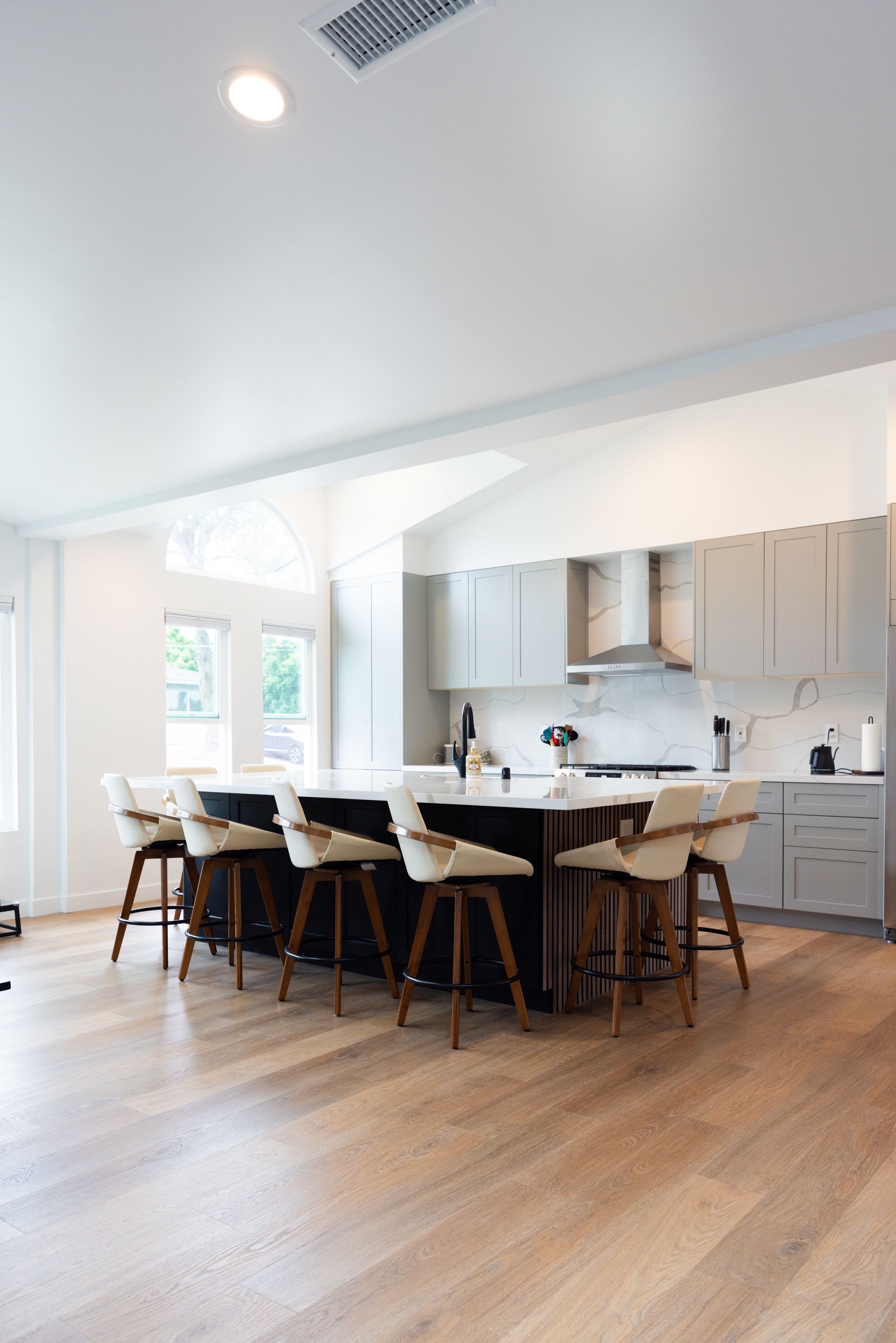 Bright modern kitchen with a large island, white cabinets, and wooden floors