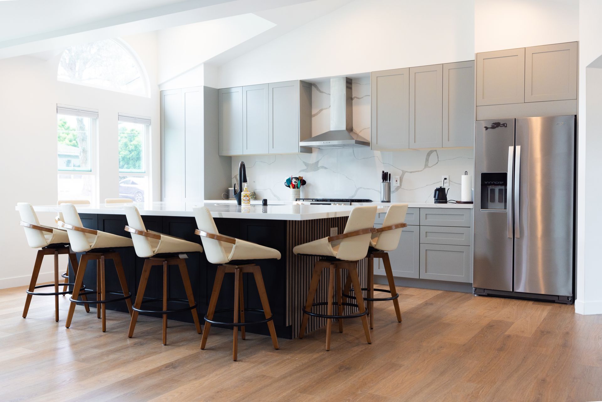 Modern white kitchen with island, bar stools, and stainless steel refrigerator