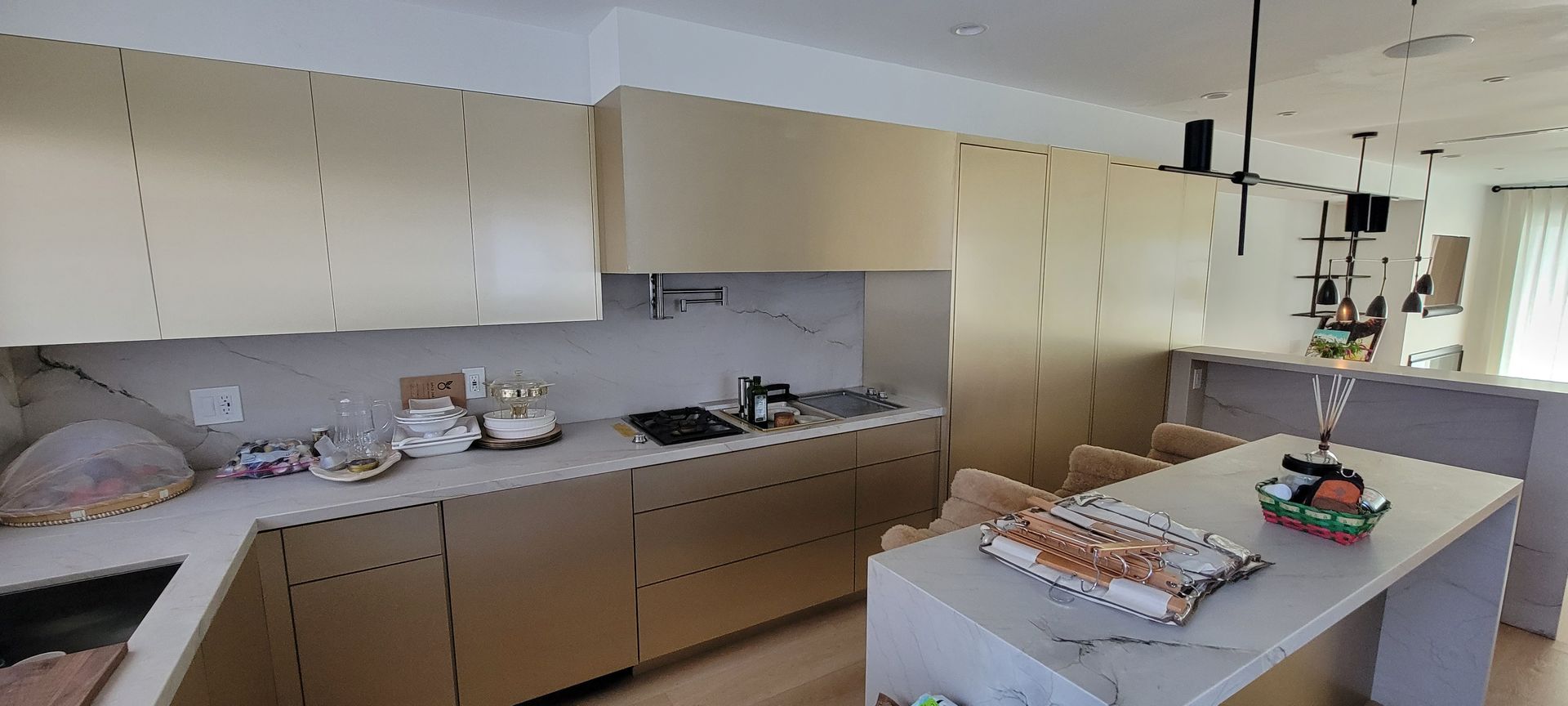 Bright kitchen with beige cabinets, cluttered countertops, and a central island with food items.