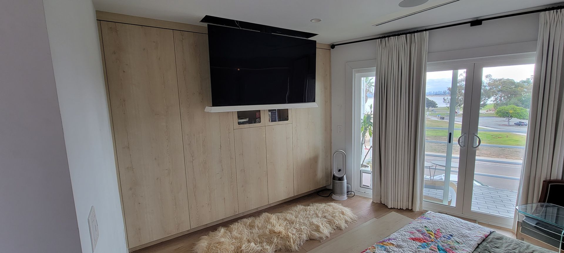 Bright room with wall-mounted TV, glass balcony doors, and a plush rug on the floor