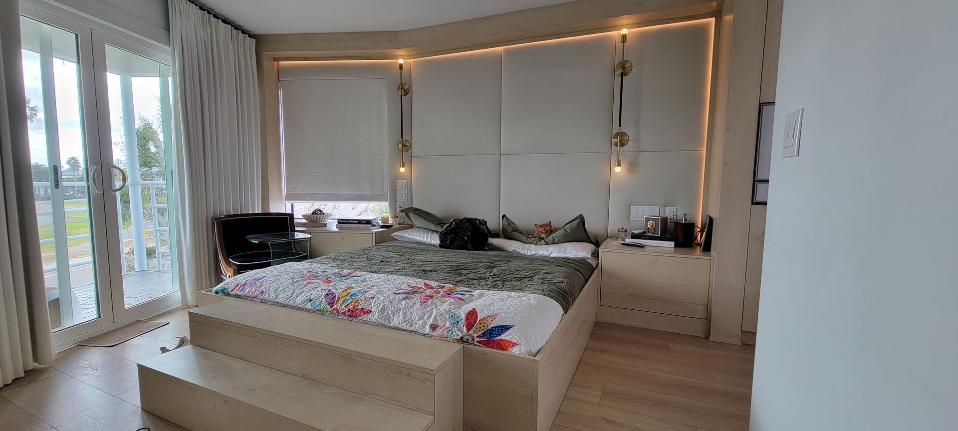 Bright bedroom with large bed, sheer curtains, warm lights, and balcony doors