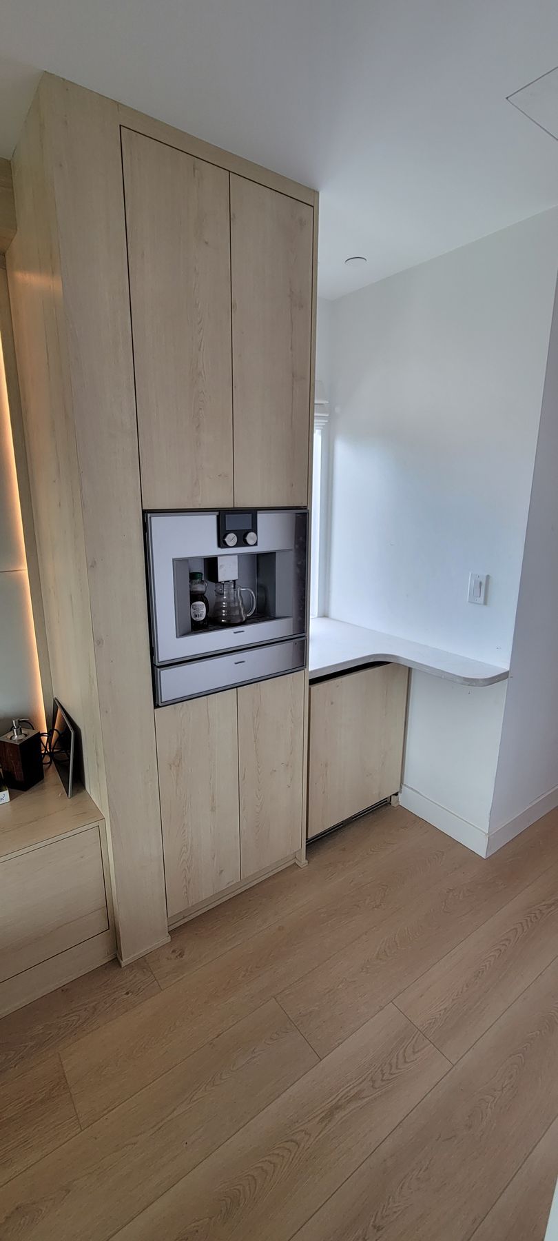 Modern kitchen with light wood cabinets, built-in oven, and white countertops on a wood floor.