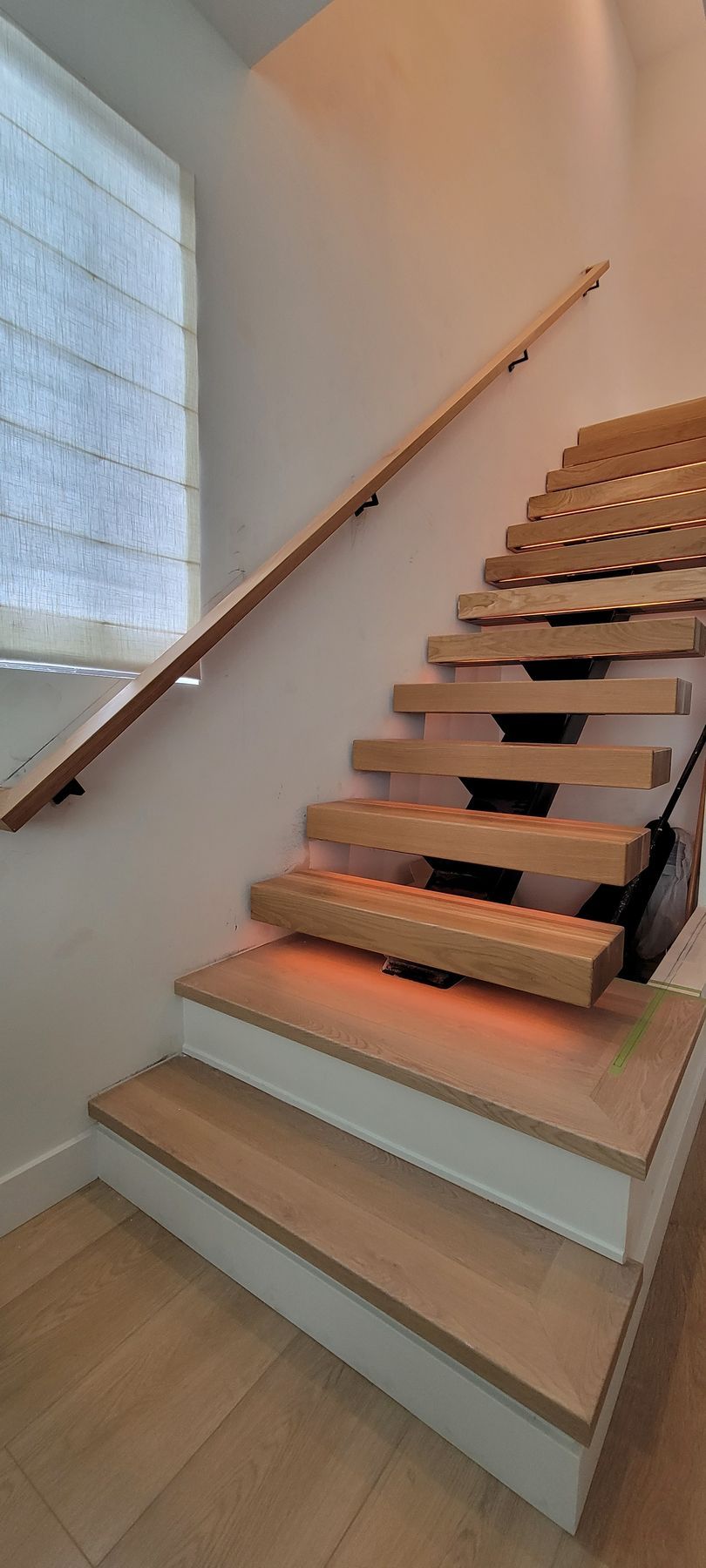 Wooden staircase with light gray steps and a handrail beside a frosted window in a bright interior