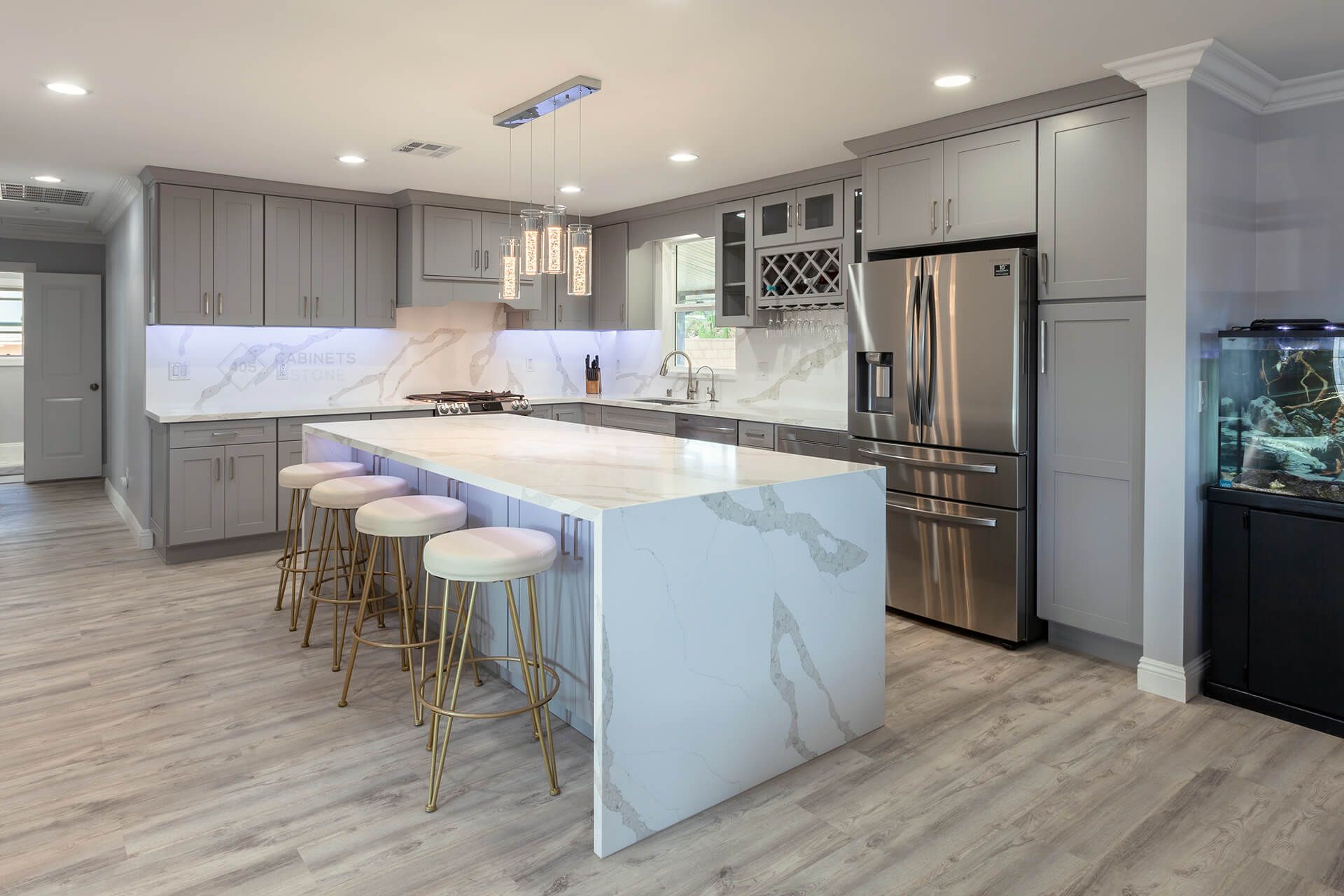 Modern kitchen with marble island, white stools, stainless appliances, and gray cabinetry