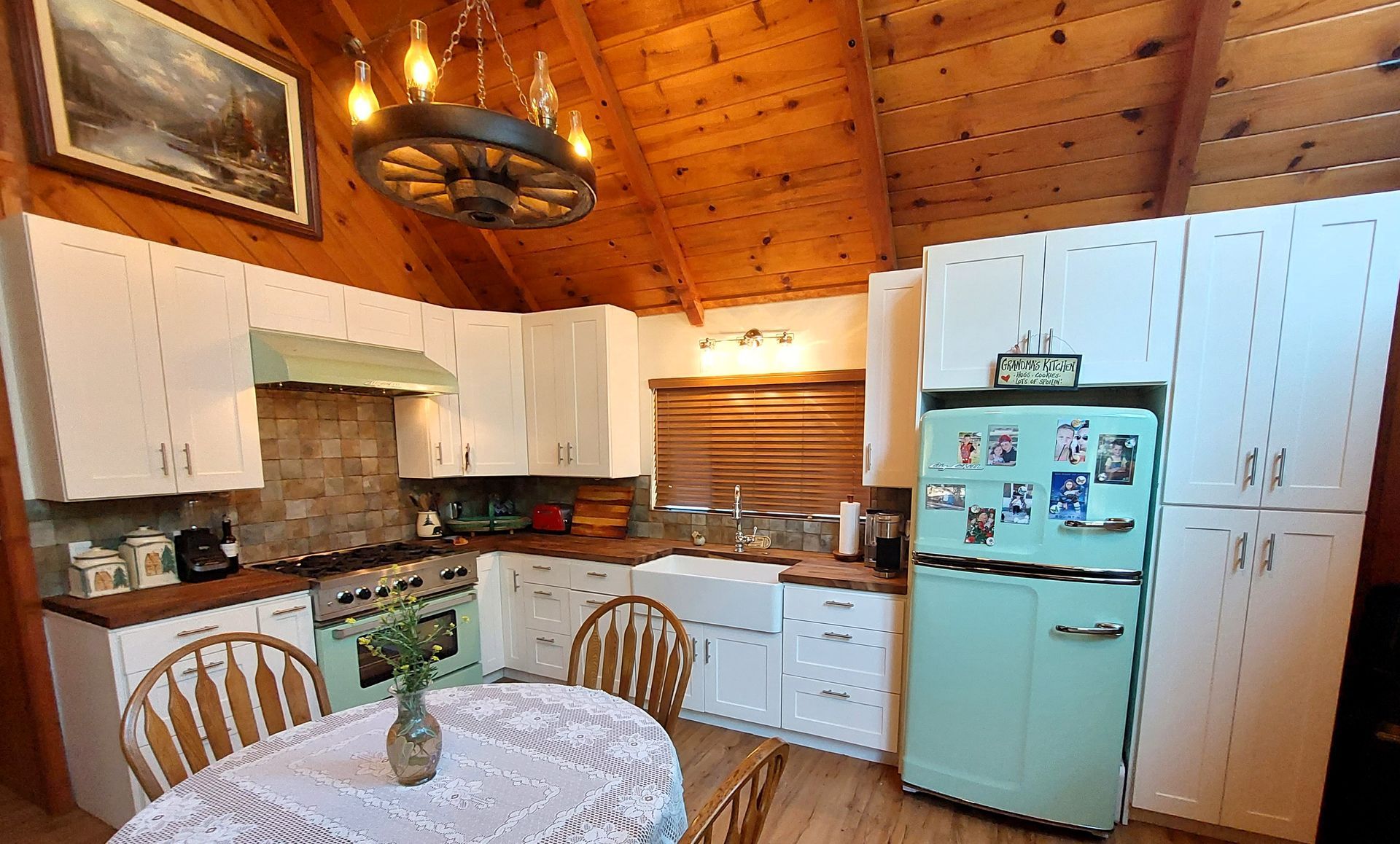 Cozy kitchen with white cabinets, wood-paneled ceiling, mint refrigerator, and round table by the window