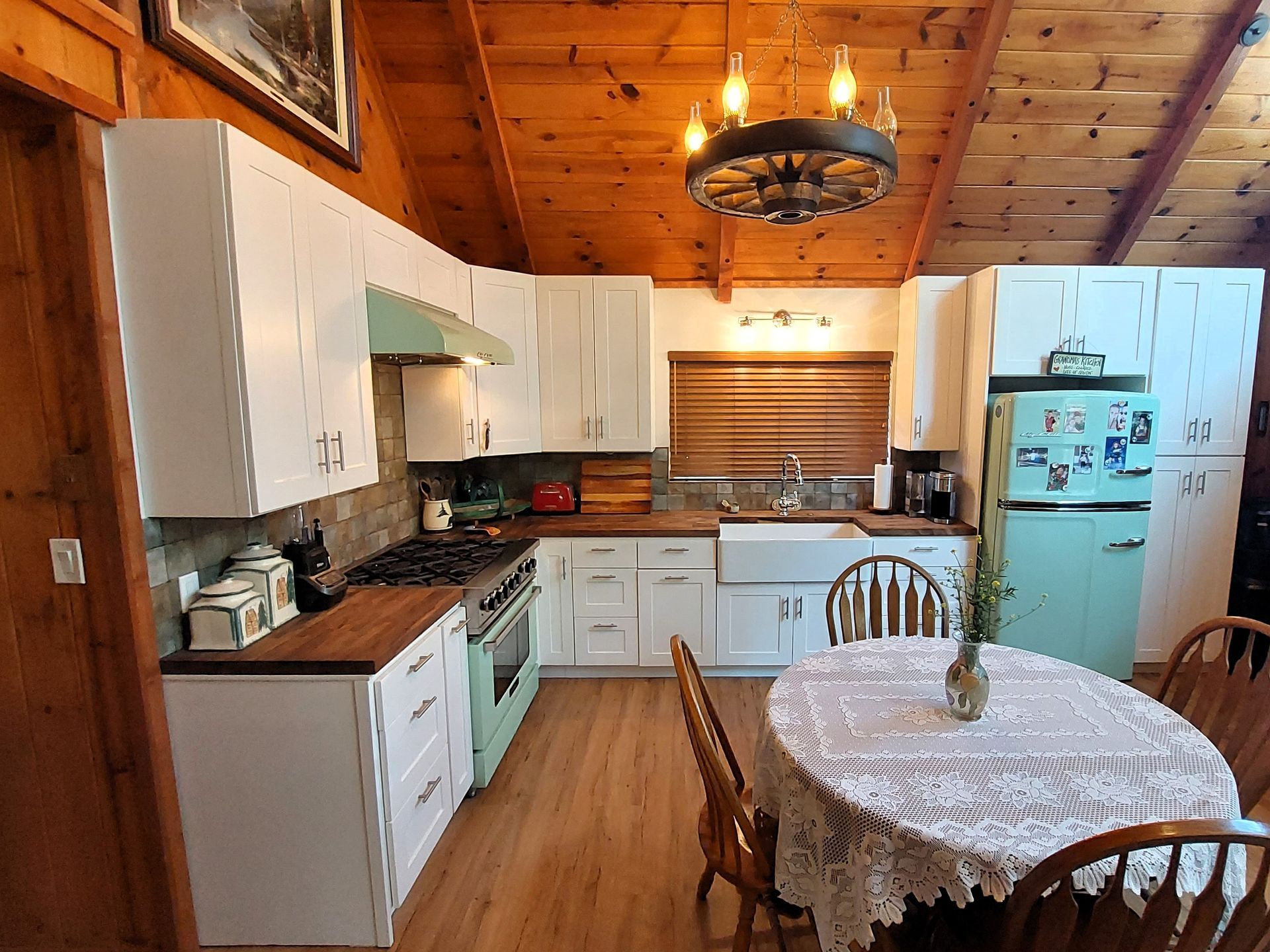 Cozy wood-paneled kitchen with white cabinets, turquoise fridge, and a round table with lace tablecloth