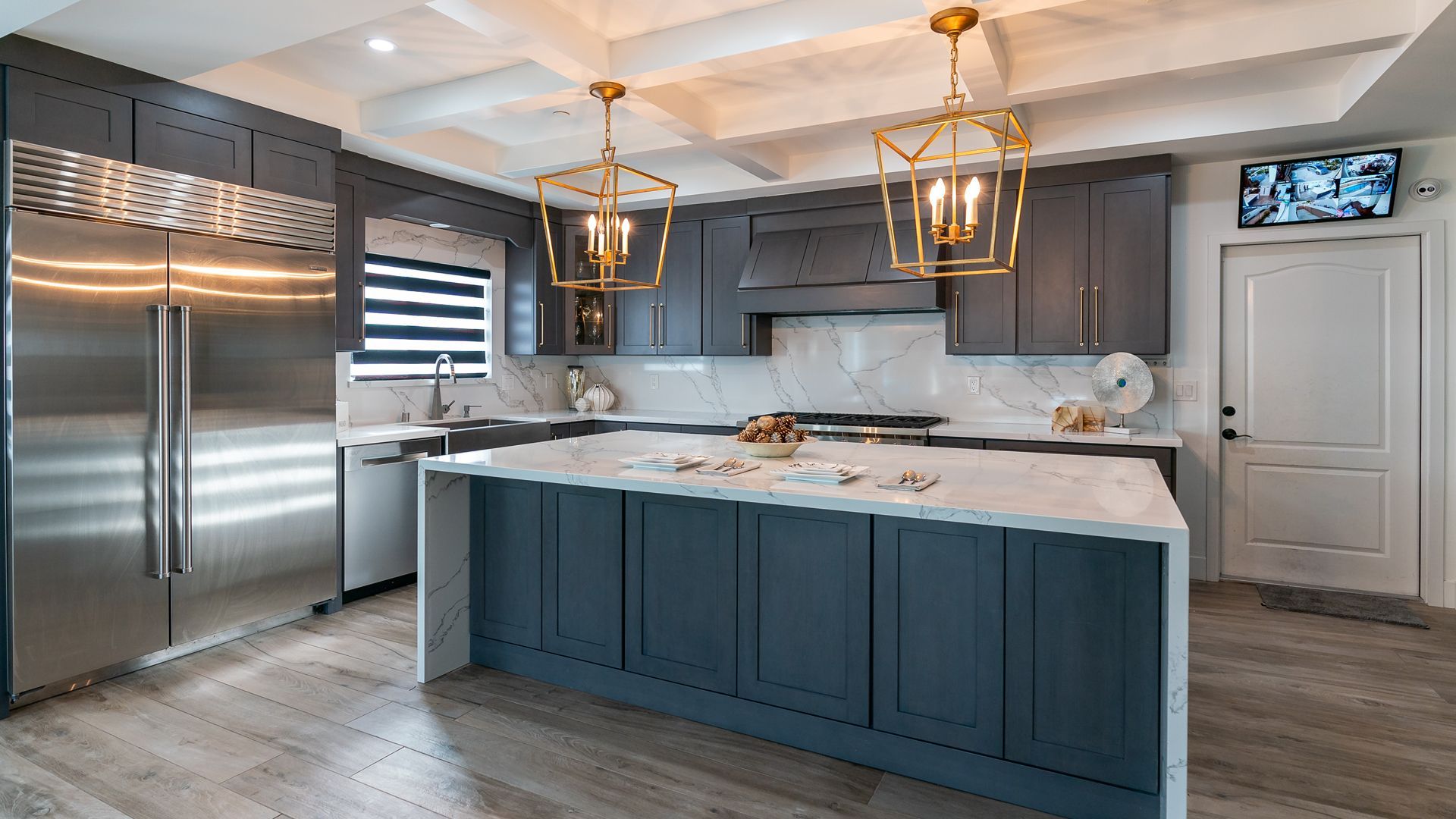 Modern kitchen with blue island, white marble counters, stainless steel fridge, and gold pendant lights