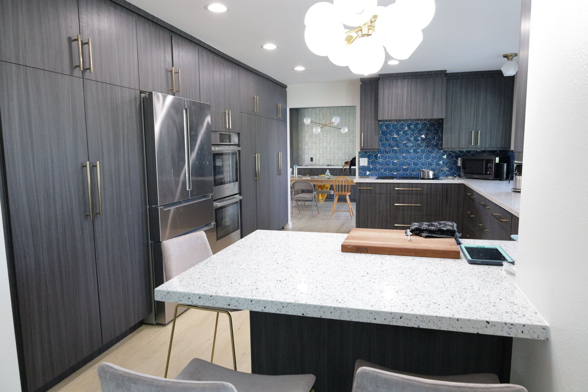 Modern kitchen with stainless fridge, dark cabinets, white island, and blue mosaic backsplash