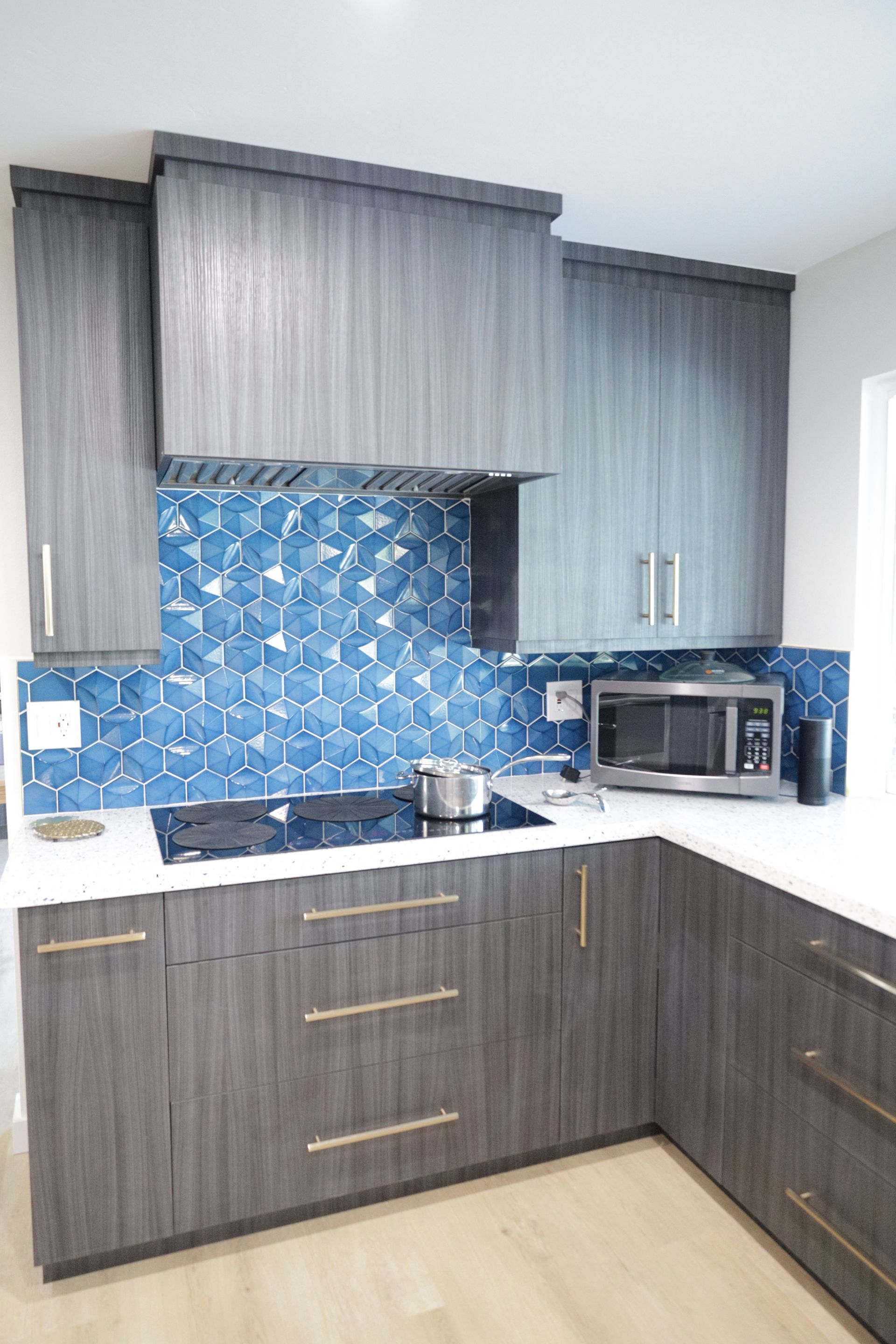 Modern kitchen with gray cabinets, blue tile backsplash, and a microwave on the counter